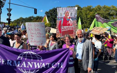 Mehrere Personen mit einem Banner von Germanwatch und einem Schild mit der Aufschrift "Ich bin hier, Ich bin laut, weil ihr mir die Zukunft klaut". Im Hintergrund wird ein großes Bild von Saúl Luciano Lliuya hochgehalten.